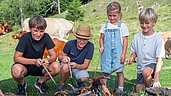 Kinder grillen Würstchen am Spieß am Lagerfeuer im Familienurlaub in Kärnten