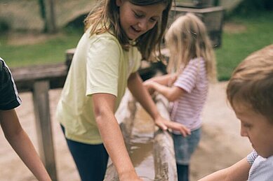 Drei Kinder spielen auf dem Außen-Spielplatz des Familienhotels Kirchheimerhof in Kärnten mit Matsch im Sand.