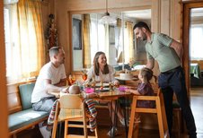 Familie mit zwei kleinen Kindern sitzt fröhlich am Esstisch, während ein Kellner im Familienhotel Sonne Bezau das Essen serviert.