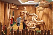 Kinder spielen im Spielbereich "Happy World" im Familienhotel Huber mit einer riesigen Murmelbahn aus Holz.