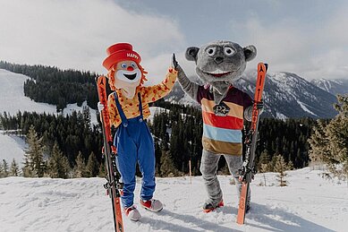 Das Familotel-Maskottchen und das Maskottchen des Familienhotels Das Bayrischzell stehen zusammen auf einem Berg