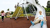 Junge rutscht die Rutsche auf dem Outdoor Spielplatz des Kolping Hotel Spa & Family Resorts hinab.