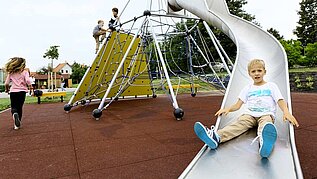 Junge rutscht die Rutsche auf dem Outdoor Spielplatz des Kolping Hotel Spa & Family Resorts hinab.