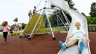 Junge rutscht die Rutsche auf dem Outdoor Spielplatz des Kolping Hotel Spa & Family Resorts hinab.