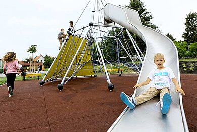 Junge rutscht die Rutsche auf dem Outdoor Spielplatz des Kolping Hotel Spa & Family Resorts hinab.