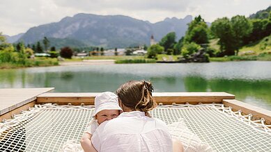 Mutter und Baby liegen auf dem Bett und schauen in die Kamera im Familienhotel Post Family Resort im Salzburger Land.