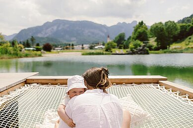 Mutter und Baby liegen auf dem Bett und schauen in die Kamera im Familienhotel Post Family Resort im Salzburger Land.