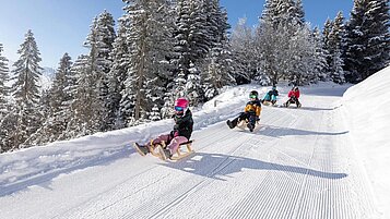 Kinder rodeln die Piste hinunter in Serfaus-Fiss-Ladis in der Nähe vom Familienhotel Adler Familien- & Wohlfühlhotel.