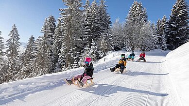 Kinder rodeln die Piste hinunter in Serfaus-Fiss-Ladis in der Nähe vom Familienhotel Adler Familien- & Wohlfühlhotel.