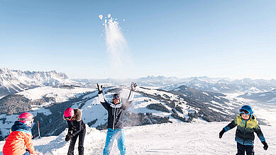 Eine Familie macht eine kurze Pause und bewirft sich mit Schnee auf der Piste nahe des Familienhotels Das Hopfgarten in Tirol.