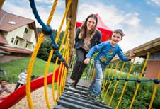 Mutter und Sohn spielen lachend auf einer Hängebrücke am Spielplatz des Familienhotel Ottonenhof.