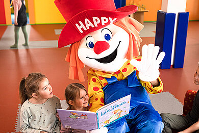 Das Familotel-Maskottchen Happy liest Kindern eine Geschichte vor