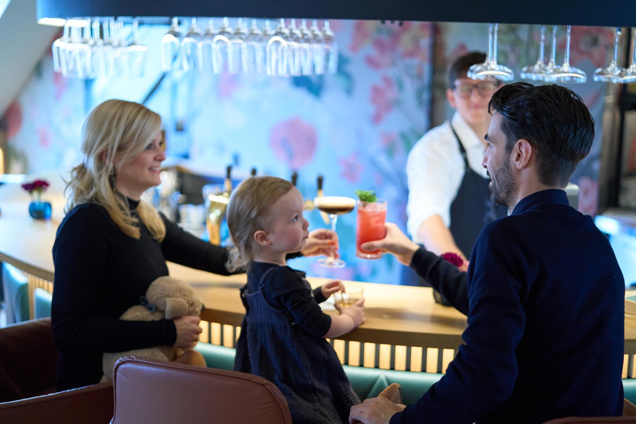 Eine Familie sitzt mit der Tochter an der Bar "Blindes Huhn" im Landhaus Averbeck und trinken einen Cocktail.